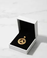 Dije circular de acero con baño dorado, con diseño central de triqueta y borde con patrón de greca.