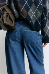 Jean de corte baggy con tiro alto, confeccionado en denim de algodón. Presenta diseño de cinco bolsillos, cierre frontal con botón y piernas con volumen en la zona de la cadera que se estrechan ligeramente hacia el bajo.