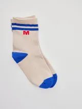 Medias de caña media color beige con rayas horizontales azules en el puño, puntera y talón en contraste azul, y detalle de letra M bordada en rojo.