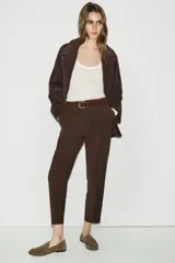 Pantalón de tiro alto en color beige, con diseño de pinzas frontales y bolsillos laterales. Incluye un cinturón a contraste en tono marrón con hebilla metálica y cierre frontal con cremallera y gancho.