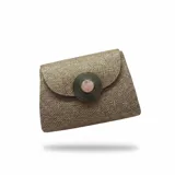 Bolso de yute de algodón color tostado, con solapa y detalle de pieza metálica circular con piedra en el centro.