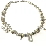 Collar de perlas sintéticas blancas y grises, con cuentas de cristal transparentes y detalles metálicos plateados. Incluye dijes de cristal en forma de punta y cierre de acero inoxidable.