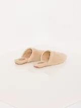 Pantuflas tipo slide color beige, confeccionadas en cuero de oveja con aplique metálico en el empeine, forrería de cuero caprino y suela de cuero vacuno.