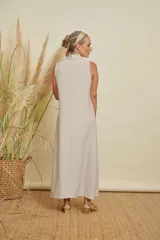 Vestido largo sin mangas, color beige claro con brillo sutil, cuello drapeado y corte recto.