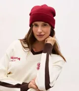 Gorro de punto de estilo beanie, color bordó, con borde plegado y etiqueta decorativa aplicada.