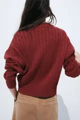 Buzo de punto trenzado en mezcla de algodón, con cuello redondo y tapeta frontal con botones. Presenta puños y bajo acanalados.