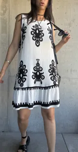 Vestido corto blanco con estampado de flores negras, corte suelto y ruedo con volantes.