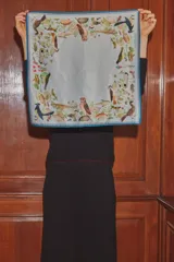 Pañuelo cuadrado de seda con estampado de fauna silvestre, incluyendo aves, peces y elementos botánicos sobre un fondo celeste, con bordes en tonos azul y rosado.