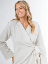 Conjunto de dos piezas confeccionado en lino color beige, compuesto por un pantalón de corte recto y un blazer cruzado con lazo ajustable en la cintura y escote en V.