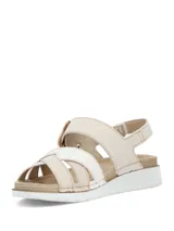 Sandalias planas de mujer en color beige, con tiras cruzadas en el empeine, una de ellas con textura plateada brilhante. Cuenta con tira ajustable al tobillo mediante hebilla con efecto carey y suela blanca con base dentada.