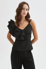 Blusa negra de poliéster con cuello en V, tirantes anchos y un diseño asimétrico con volados escalonados en un hombro. Corte entallado.