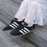 Championes Adidas modelo Gazelle Lo Pro, color negro con las tres tiras laterales en blanco y suela de goma color caramelo. Presenta el logo de la marca y el nombre del modelo en dorado en el lateral.