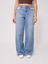 Jean de corte baggy y tiro medio, confeccionado en denim de algodón en tono azul claro con efecto lavado. Presenta diseño de cinco bolsillos, cierre frontal con botón y cremallera, y pernera ancha.