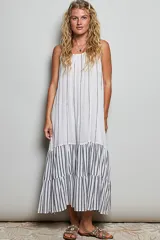 Vestido largo sin mangas de color blanco con rayas verticales oscuras, corte holgado y diseño con volantes en la parte inferior.