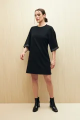 Vestido corto color rosa nude de punto, con mangas cortas y apliques de tachas plateadas en las terminaciones de las mangas.