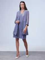 Conjunto de fiesta marca RM Richards, compuesto por vestido corto azul marino de seda fría con apliques bordados y chaqueta de seda fría con apliques bordados y mangas de microtul. El vestido tiene corte recto y largo a la rodilla. La chaqueta es abierta, con mangas 3/4 y largo a la cadera. El conjunto tiene forro interno a tono.