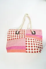 Bolso de playa o tote bag con diseño de patchwork en tonos rosados, naranjas y blancos. Presenta secciones con estampado de lunares rojos y secciones con tejido de rafia. Las asas son de cuerda trenzada.