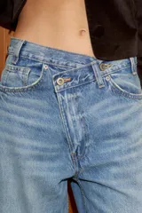 Jeans de tiro alto, color gris oscuro lavado, con pierna ancha extra larga (full length) y diseño de cintura cruzada asimétrica con cierre frontal de cremallera y botones metálicos.