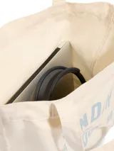 Bolso tipo tote de lona color crema con estampado gráfico de la marca Under Armour en color azul claro. Cuenta con un amplio compartimento principal y correas para llevar al hombro.