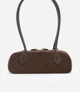 Cartera tipo shoulder bag de tamaño pequeño y formato alargado, confeccionada en material sintético efecto gamuza. Cuenta con asas de hombro estructuradas, cierre superior con cremallera y detalles metálicos decorativos.