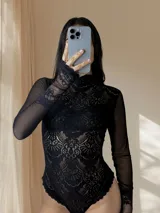 Body de encaje y microtul color negro, con mangas largas, cuello alto y diseño entallado que combina transparencias.
