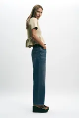 Chaqueta de punto color beige claro, con cuello redondo, manga corta y bajo peplum con pliegues. Cierre frontal con botones forrados a tono.