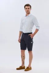 Bermuda cargo color azul marino, de gabardina con bolsillos laterales con solapa en las piernas y presillas para cinturón. Incluye cinturón de lona trenzada oscura con detalles en cuero sintético y hebilla metálica.