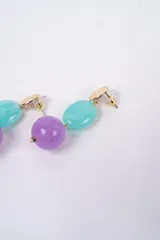 Caravanas colgantes con diseño de tres piezas: un disco superior dorado con textura estriada, una cuenta ovalada de resina roja y una cuenta esférica de resina verde jaspeada en la parte inferior.