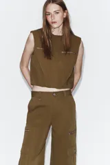 Pantalón cargo de tiro alto en color marrón tostado, con diseño de pernera holgada que se estrecha hacia el tobillo. Presenta bolsillos frontales con cierre de cremallera, bolsillos laterales de plastrón con solapa y botón, y cierre frontal con cremallera y botón.