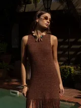 Vestido corto tejido a mano en crochet, color marrón con destellos metalizados. Presenta escote redondo, diseño sin mangas y un ruedo con flecos largos que aportan movimiento.
