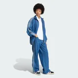 Chaqueta deportiva Adidas Firebird Adilenium de denim, color azul, con cuello alto, cierre frontal y las clásicas tres tiras en las mangas. Cuenta con bolsillos frontales ribeteados y el logo del trifolio bordado en el pecho.