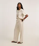 Pantalón largo de cintura alta color beige, confeccionado en tejido viscolino, con trabillas en la cintura, cinturón de cuerda para lazo, cierre tradicional y pliegues.