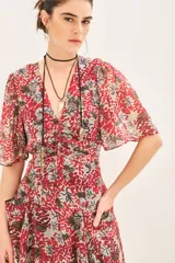 Vestido corto con estampado floral en tonos rojo/fucsia y gris/azul, escote en V, mangas cortas con vuelo y frunces en el delantero y espalda. Posee bolsillos delanteros.