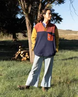 Buzo polar de diseño color block con mangas amarillas, cuerpo azul marino y detalle superior en color terracota. Presenta cuello alto con cierre de botones a presión y un bolsillo frontal con solapa y cierre a presión en el pecho. Confeccionado en tejido polar fleece sintético.