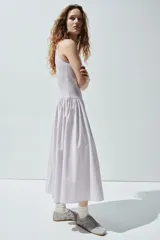Vestido midi sin mangas confeccionado en sirsaca de algodón color lila, con cuerpo ajustado de punto smock, escote redondo y falda amplia con vuelo y costura fruncida en la cadera.