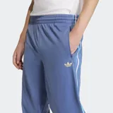 Pantalón de jogging azul con cintura elástica ajustable con cordón, bolsillos laterales con cierre y logo Adidas bordado en dorado. Presenta las tres tiras clásicas de Adidas en blanco y celeste a lo largo de la pierna.
