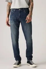 Pantalón de jean azul oscuro, corte slim fit, con pierna cónica y tiro medio. Diseño clásico de cinco bolsillos.