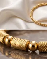 Pulsera tipo esclava rígida de acero con baño de oro, con diseño de eslabones texturizados y esferas lisas intercaladas.