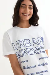 Remera de manga corta color beige, con estampa frontal en tono azul con la leyenda "New York 1990", de corte holgado y diseño casual.