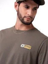 Remera de manga corta y cuello redondo color verde oliva. Presenta un pequeño estampado rectangular en el pecho con el logo de la marca y herramientas cruzadas, además de un diseño gráfico en la espalda.