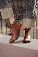 Botín de cuero negro, caña corta, con punta cuadrada y cierre lateral. Presenta un tacón de madera de altura media y detalles en charol con textura de cocodrilo en el talón.