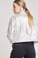 Cazadora estilo biker metalizada en color plateado, con cierre frontal asimétrico, solapas con broches a presión, mangas largas con cierre en los puños y cinturón ajustable en el ruedo.