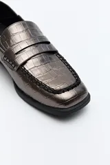 Mocasín de cuero sintético negro con punta cuadrada, detalle de costuras visibles en la capellada y taco bajo.