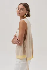 Chaleco tejido de algodón color beige, con escote en V, lazos laterales y terminaciones con pompones.