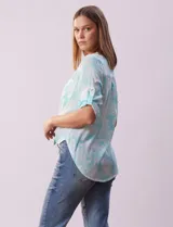 Blusa celeste con estampado blanco, de gasa, con cuello a la base y escote en V. Tiene abertura con botones, bolsillos delanteros y mangas 3/4 regulables con presilla y botón. El ruedo termina con un nudo.
