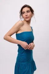 Vestido azul con bretel fino, escote asimétrico de un hombro, corte a la cintura con recorte en el lateral y falda midi con volados irregulares.