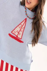Buzo de punto color celeste con cuello redondo y diseño frontal de un velero tejido en tonos rojos y blancos, con detalles bordados a mano.