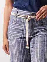 Pantalón de lino a rayas verticales en tonos azul, beige y blanco, con corte wide leg, pretina con pasadores, cierre y botón. Incluye cinturón de soga con hebilla redonda.