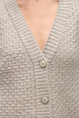 Cardigan de tejido de punto con textura, silueta boxy y cuello en V. Presenta cierre frontal con botones y detalles de terminación en contraste de color en los bordes.