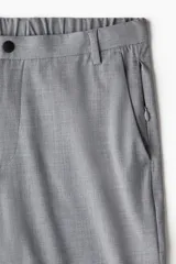 Pantalón de corte slim fit en color gris, con cierre frontal de cremallera y botón, bolsillos laterales y bolsillo trasero insertado.